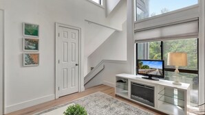 Un salon moderne avec un escalier, un téléviseur et des œuvres d’art accrochées aux murs.