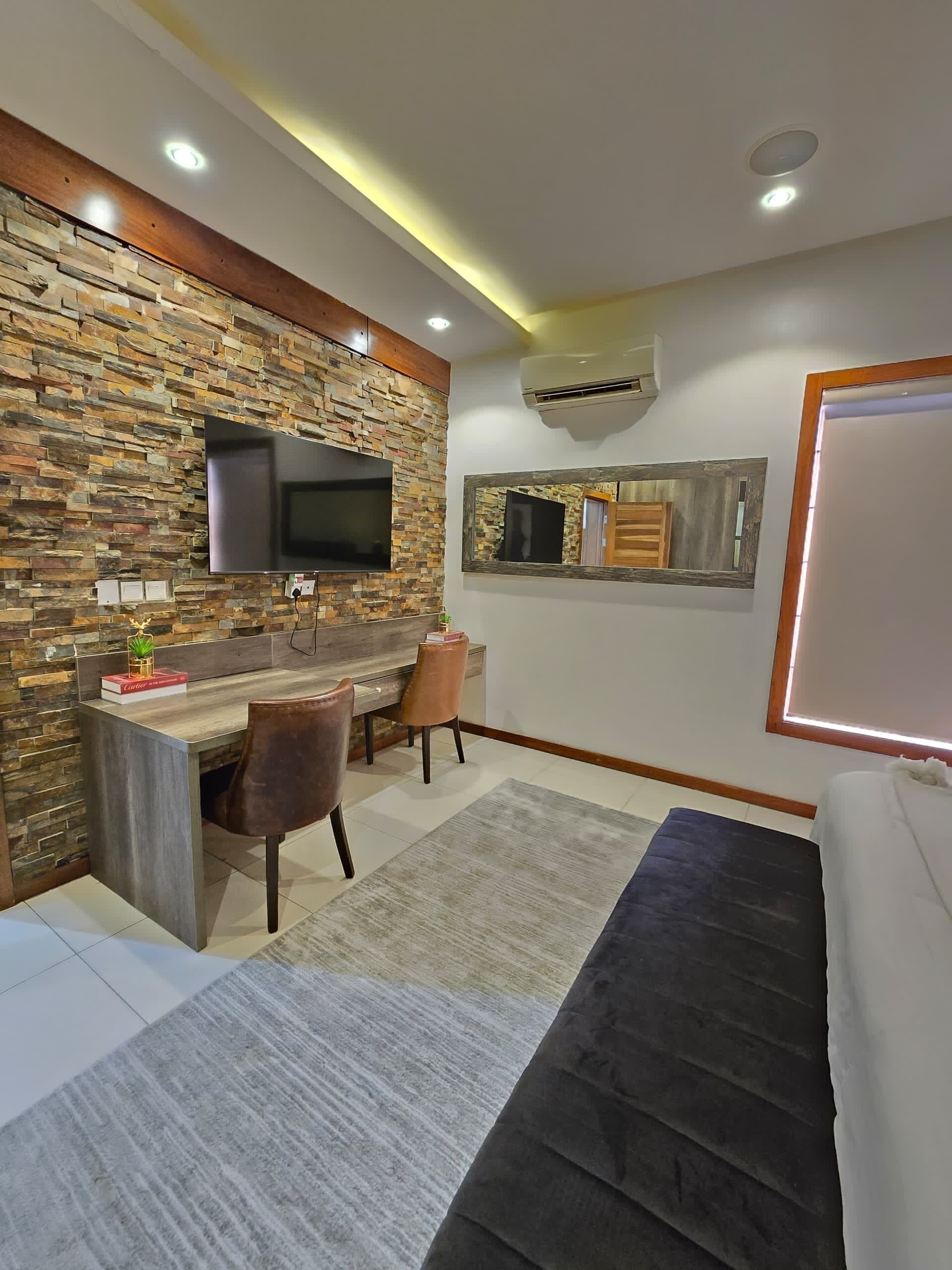 Une chambre moderne avec un mur en pierre, un téléviseur à écran plat, un bureau avec une chaise, un lit et un escalier.