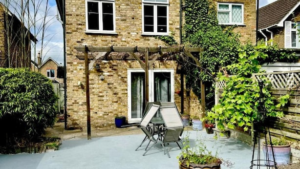 Uma casa de dois andares com um pátio, uma pérgola e um jardim.