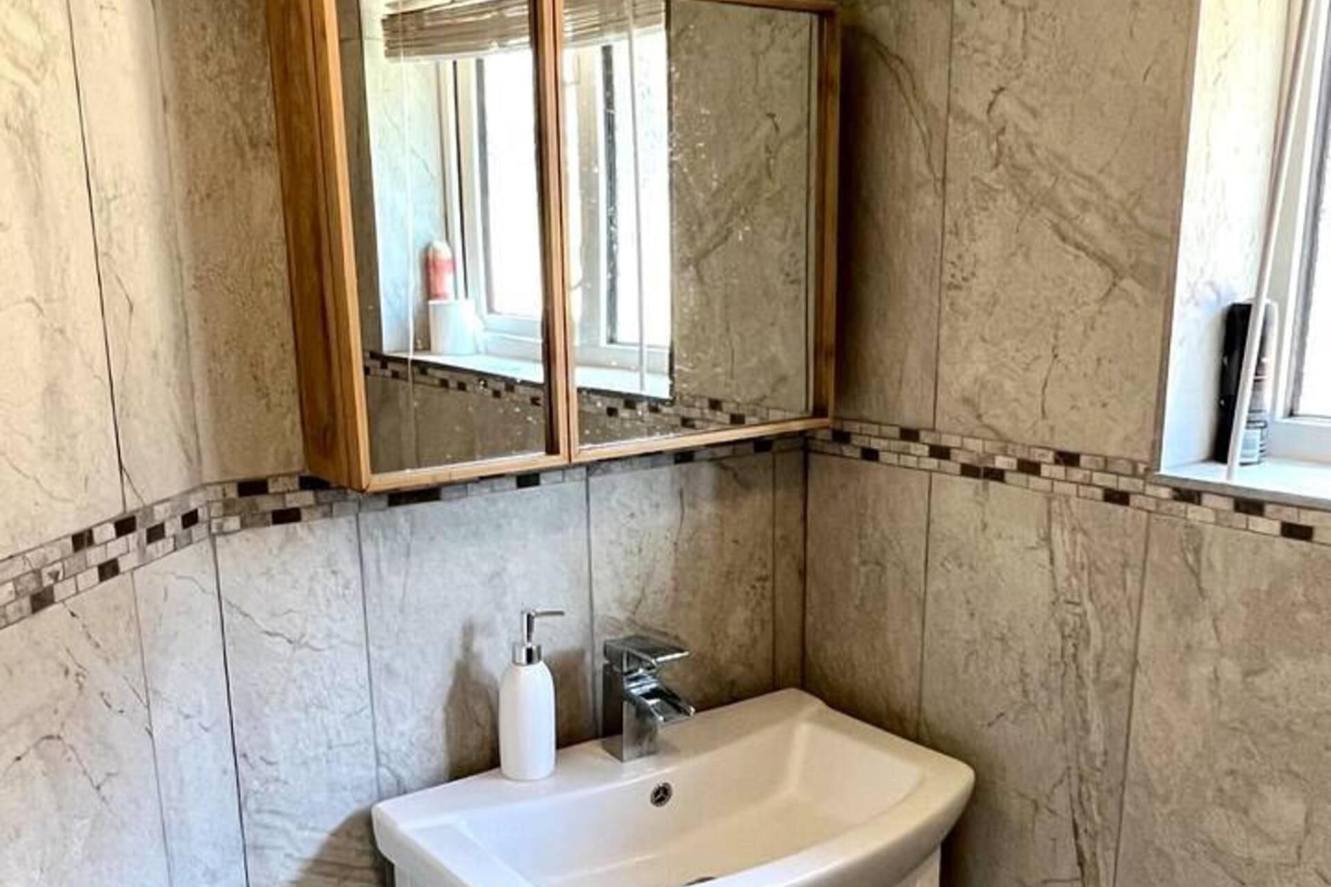 Ein Badezimmer mit weißem Waschbecken, einem Spiegel und einer gefliesten Rückwand.