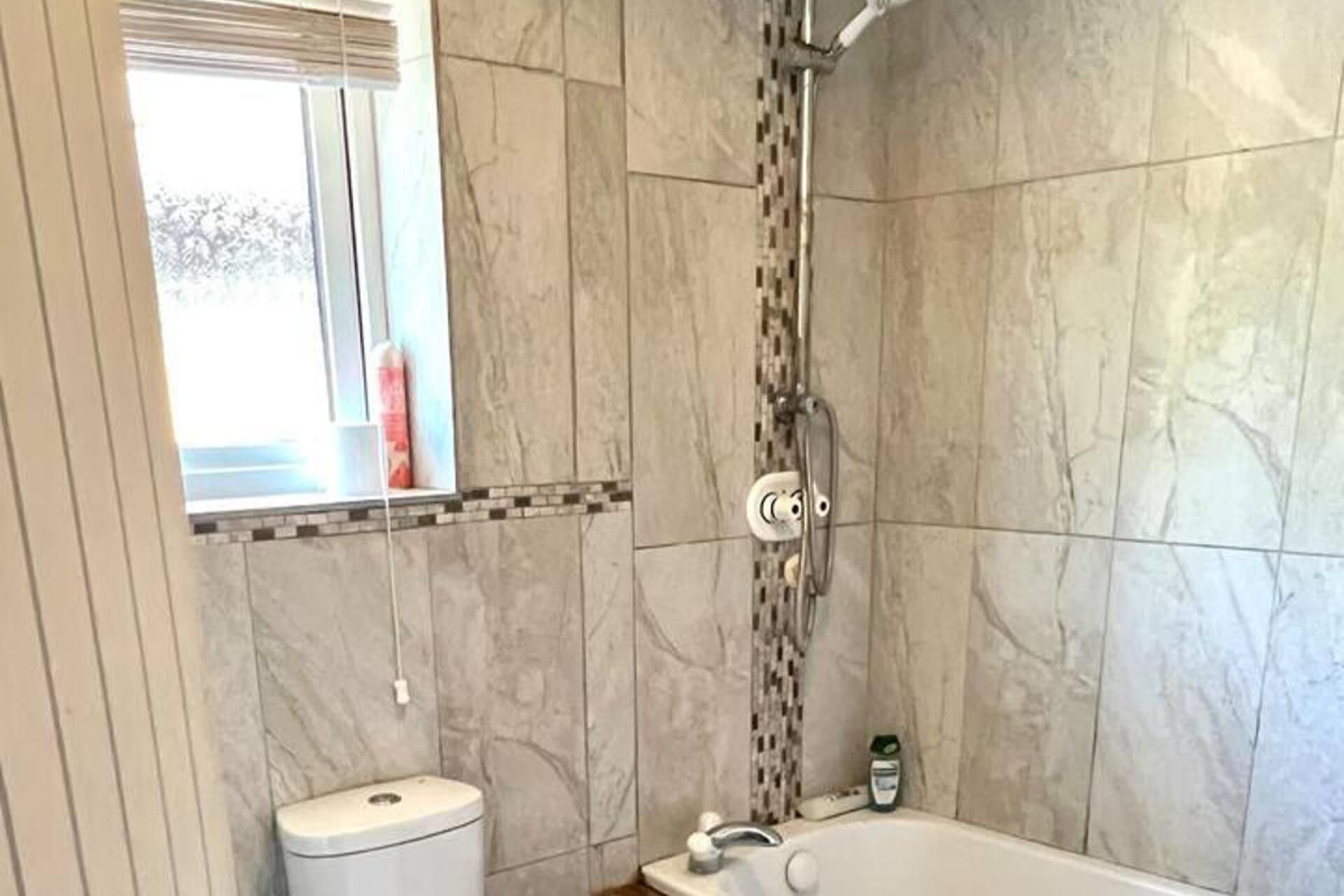 A bathroom with a shower, toilet, and a window.