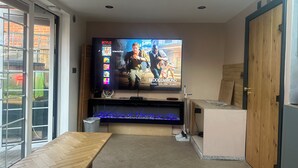 A living room with a flat-screen TV mounted on the wall, a wooden table, and a fish tank. - Stunning 1-bed Studio in London (London)
