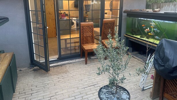 A patio area with a glass door leading to a room, two wooden chairs, a small potted plant, and a fish tank. - Stunning 1-bed Studio in London (London)