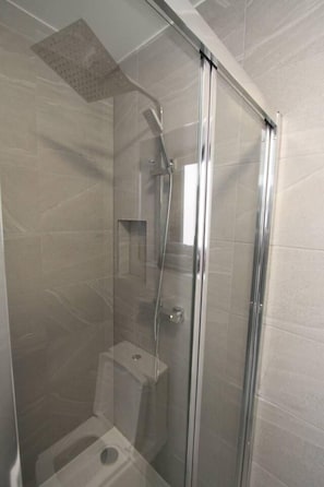 Shower area features a glass door, wall-mounted showerhead, and a shower control panel.