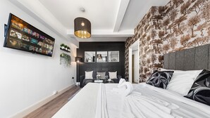 Une chambre d’hôtel moderne dotée d’un grand lit, d’un téléviseur à écran plat fixé au mur, d’un papier peint au motif original et d’un élégant luminaire suspendu.