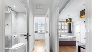 Une salle de bain moderne équipée de toilettes, d’une douche et d’un lavabo. La pièce est dotée d’un plancher en bois et de murs blancs.