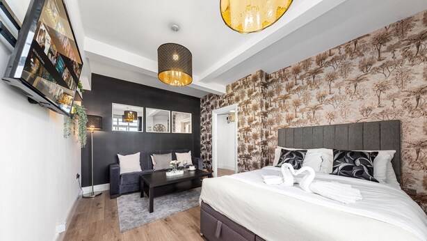 Une chambre à coucher moderne avec un grand lit, des éléments de décoration murale aux couleurs sombres et un papier peint à motifs d’arbres originaux.