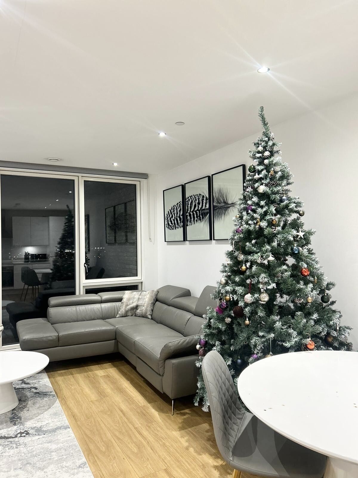A modern living room with a large gray sectional sofa, a white round table, and a decorated Christmas tree.