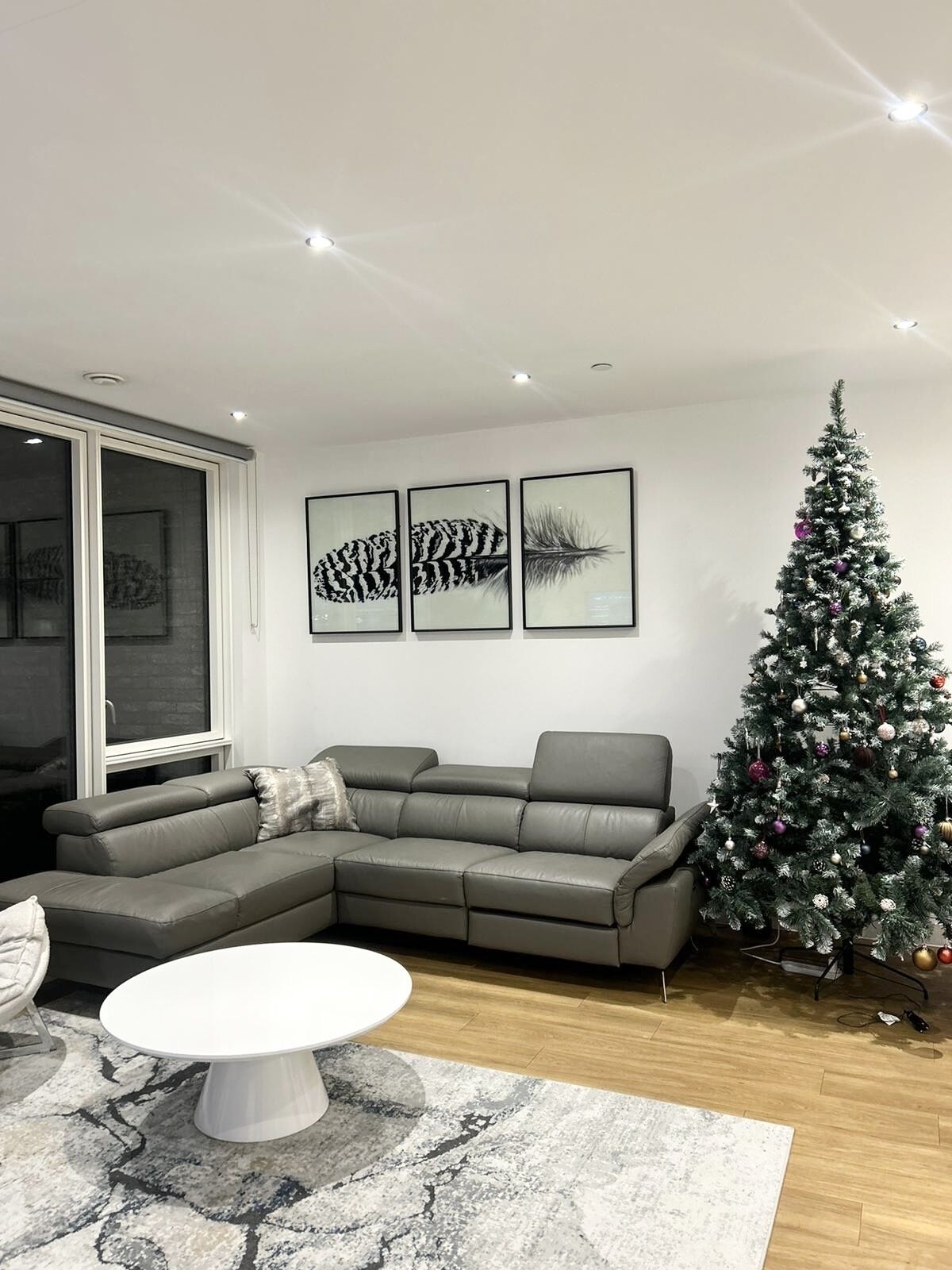 A modern living room with a grey sectional sofa, a white coffee table, and a Christmas tree.
