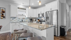A modern kitchen with white cabinets, stainless steel appliances, and a granite island with bar stools. - Lakefront Paradise: 3 BR Lodge with Private Hot Tub, Indoor/Outdoor Pool Access! (Hollister)