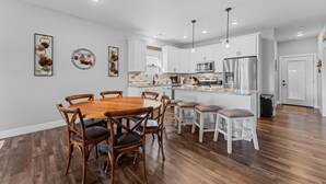 A modern kitchen with white cabinets, a stainless steel refrigerator, and a wooden dining table with chairs. - Lakefront Paradise: 3 BR Lodge with Private Hot Tub, Indoor/Outdoor Pool Access! (Hollister)