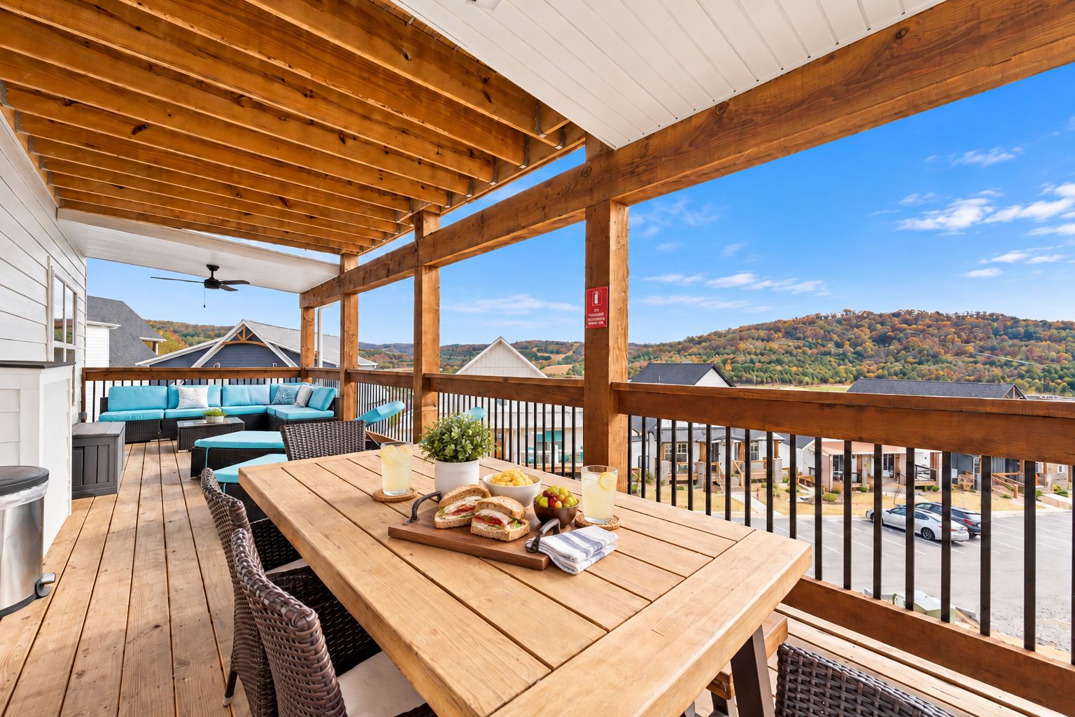 A wooden deck with outdoor furniture, a table with food and drinks, and a view of a hilly landscape.