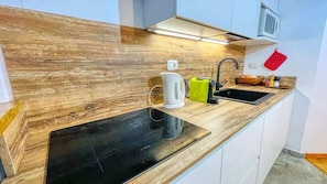 Uma cozinha moderna com painel de madeira, fogão por indução preto, chaleira, pia e micro-ondas.