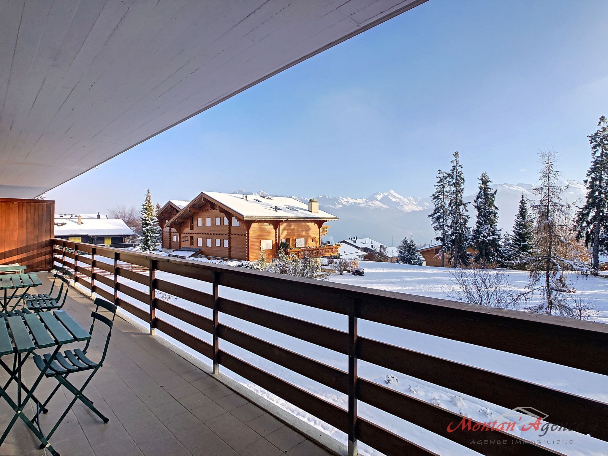 Ein Holzbalkon mit Blick auf ein Berghaus und eine verschneite Landschaft.
