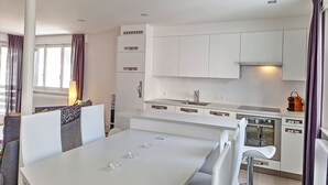 A modern kitchen with white cabinets, a central island, and a dining area with a white table and chairs.