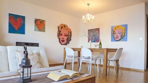 Una sala de estar con un sofá, una mesa de centro con un libro abierto, una araña y un comedor con sillas y una mesa.