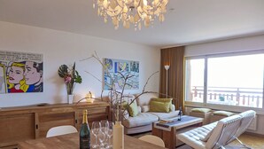 Una sala de estar moderna con una mesa de comedor de madera, una araña, un sofá y un balcón con vistas.