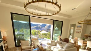 A spacious living room with a large window offering a mountain view, a round wooden coffee table, and a chandelier.
