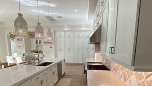 A modern kitchen with white cabinetry, a large island, pendant lights, and a patterned backsplash.