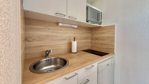Une cuisine compacte dotée d’un évier en acier inoxydable, d’un plan de travail en bois, de meubles blancs et d’un four à micro-ondes placé au-dessus de l’évier.