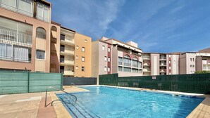 Une piscine à l’eau d’un bleu cristallin, entourée d’immeubles à plusieurs étages dotés de balcons.