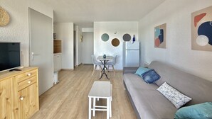 Un salon moderne comprenant un canapé, une petite table, un téléviseur et un coin cuisine avec un réfrigérateur et des placards.