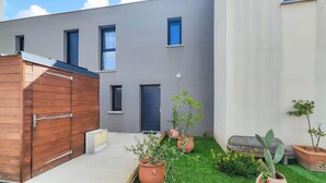 A modern building with a grey facade, a wooden gate, and a small garden with potted plants and a cactus. - Pet friendly home in Agde with WiFi (Agde)