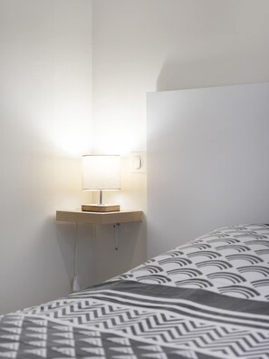 Una cama con un edredón estampado, una mesita de noche con una lámpara y una pared blanca.