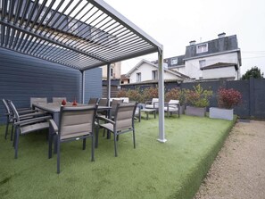 A patio with a table and chairs, a pergola, and a well-maintained lawn.