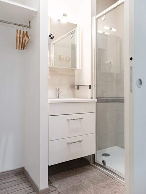 Un baño moderno con cabina de ducha de vidrio, tocador blanco con cajones y un perchero para toallas.