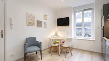 Un espace de vie compact comprenant un coin repas, un téléviseur fixé au mur et une fenêtre donnant sur l’extérieur.