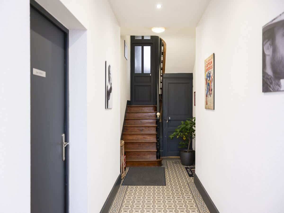 Un couloir étroit avec un escalier en bois, une plante en pot et un tapis à motifs.