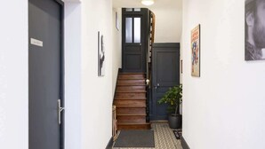 Un pasillo estrecho con una escalera de madera, una planta en maceta y una alfombra estampada.