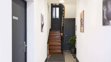 Un couloir étroit avec un escalier en bois, une plante en pot et un tapis à motifs.