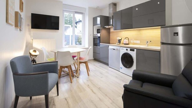 Una cocina moderna con lavadora, comedor con sillas y un televisor de pantalla plana montado en la pared.