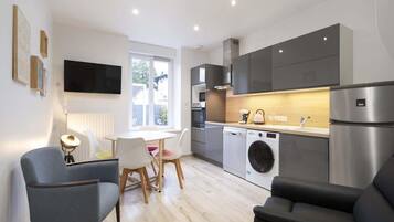 Une cuisine moderne équipée d’un lave-linge, d’un coin repas avec des chaises et d’un téléviseur à écran plat fixé au mur.