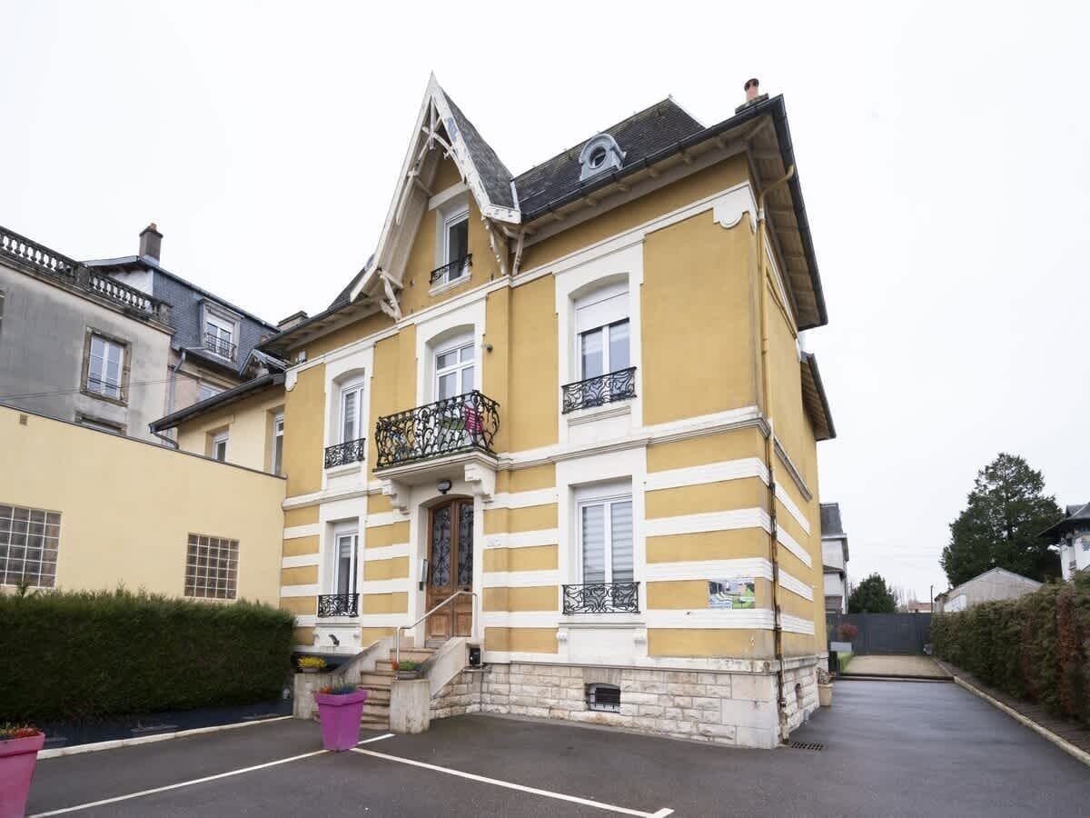 Un bâtiment jaune doté d’un balcon, d’une entrée en pierre et d’un espace de stationnement.