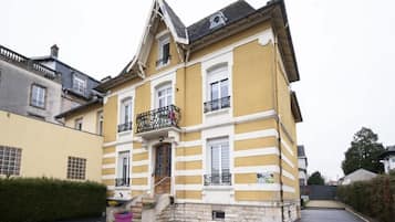 Un bâtiment jaune doté d’un balcon, d’une entrée en pierre et d’un espace de stationnement.
