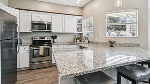 A modern kitchen with white cabinets, stainless steel appliances, granite countertops, and a large window with blinds. - Sandpiper Cove unit 9138 with beach service (Destin)