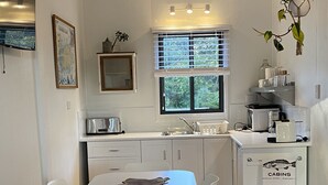 Una cocina moderna con armarios blancos, una mesa de comedor con sillas, un ventanal con persianas y una planta colgante.