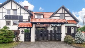 A two-story house with a tiled roof, a black gate, and a paved driveway.