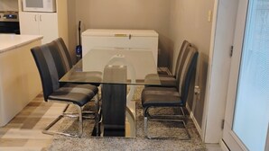 A dining area with a glass table, four chairs, a white refrigerator, a microwave, and a chandelier. - The Beautiful Nubia - 5 Mins Drive to the Calypso Waterpark.  (Limoges)