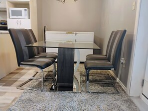 A dining area with a glass table, four chairs, a microwave, and a white cabinet.