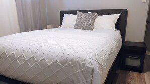 A neatly made bed with a white quilt, a dark headboard, and a small bedside table. - The Beautiful Nubia - 5 Mins Drive to the Calypso Waterpark.  (Limoges)