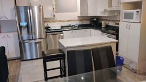 A modern kitchen with stainless steel appliances, white cabinetry, a glass dining table, and a black chair. - The Beautiful Nubia - 5 Mins Drive to the Calypso Waterpark.  (Limoges)