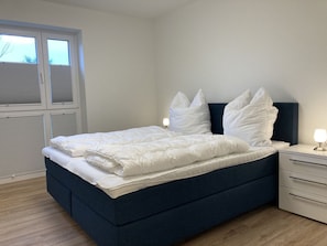 A neatly made bed with white bedding and pillows, a dark blue headboard, and a bedside table with a lamp. - Dahmer Dünen - Ostseezauber - Dahmer Dünen - Ostseezauber! (Dahme)