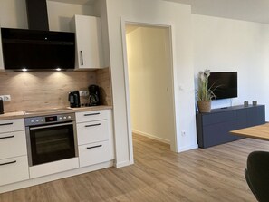 A modern kitchen with white cabinetry, a built-in oven, a coffee maker, and a TV on a dark cabinet. - Dahmer Dünen - Ostseezauber - Dahmer Dünen - Ostseezauber! (Dahme)