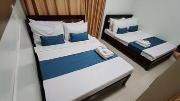 Two single beds with white and blue bedding, a wooden headboard, and a curtain.
