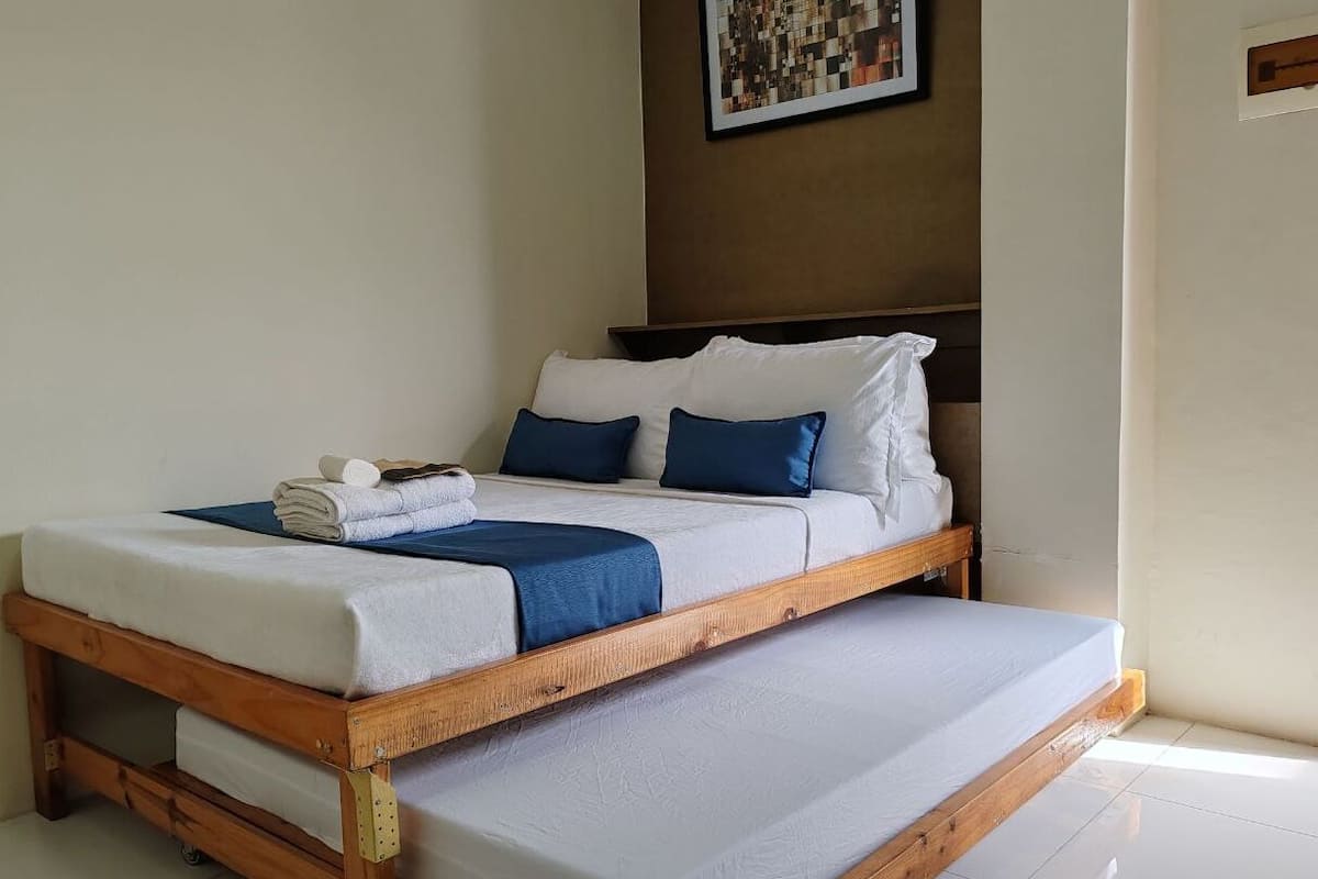 A single bed with a wooden frame, white bedding, and blue pillows.