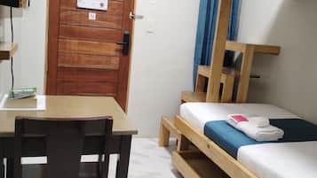 Una habitación con un escritorio de madera, una cama litera con ropa de cama azul, una puerta de madera con un letrero y un estante pequeño.
